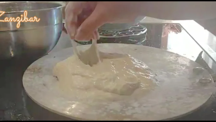 Take a portion of the dough (palm-sized), flatten it slightly, and place it on the hot pan. Sprinkle sesame seeds on top. Spread it using your fingers.