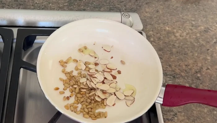 Lightly saute pine nuts and almonds in olive oil until browned.