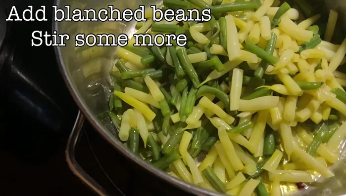 Add blanched green beans to the pot and stir until heated through and evenly coated with spices.