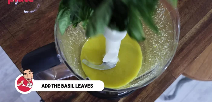 Add basil and blend: Add basil leaves to the blender. Blend until the basil is finely chopped and combined with the oil and nut mixture.