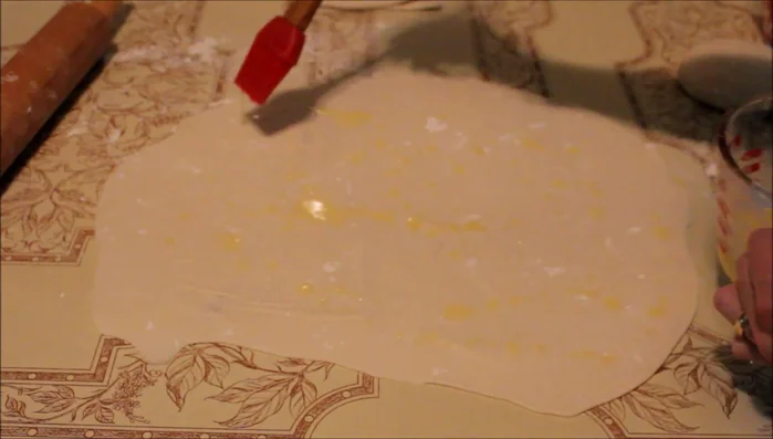Sprinkle melted butter on one side of the dough. Fold the dough in thirds lengthwise, then fold again to create three layers.