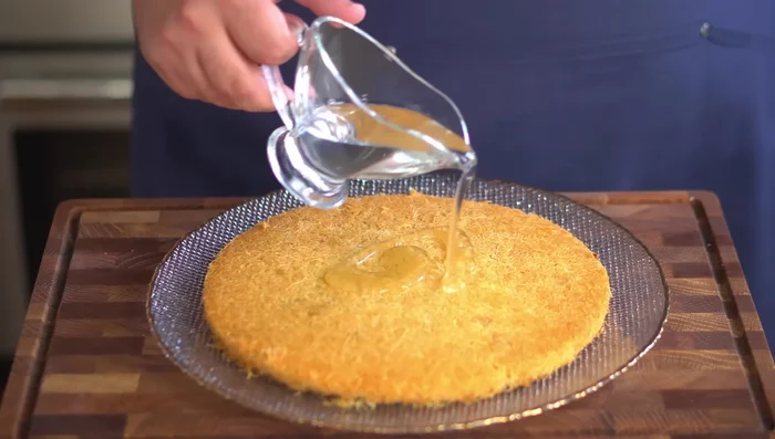 Pour simple syrup (recipe in description) evenly over the kunafa.