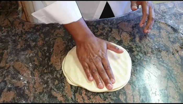 Layer the oiled rotis: Press down one, then flip and press again. Apply dry flour, roll out gently, adding more flour as needed.
