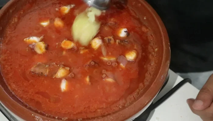 Add the diced octopus, garlic paste, 1 tbsp of homemade harissa, 1 tbsp cumin, 1/2 tbsp paprika, 1 tsp black pepper, 1 tsp salt, and a portion of the boiling octopus water. Mix everything together.