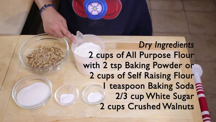 Gather all dry ingredients: 2 cups all-purpose flour (or 2 cups self-raising flour), 2 teaspoons baking powder (or 1 teaspoon baking soda), 2/3 cup white sugar, and 2 cups crushed walnuts.