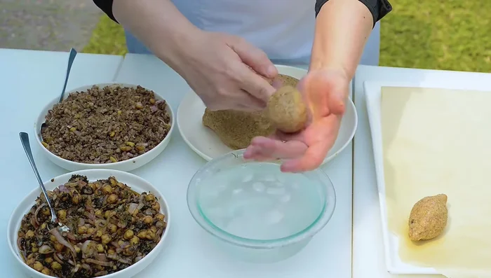 Dampen hands with ice water. Take a handful of kibbeh dough (egg-sized), create a well in the center, and shape into a thin-walled cup (2mm thick).
