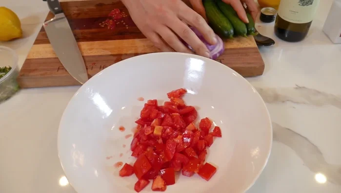 Combine the cubed tomatoes, red onion, and cucumbers in a bowl.
