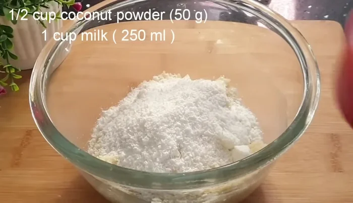 Add coconut powder, milk, baking powder, and vanilla essence. Mix well and let it rest for 5-7 minutes.