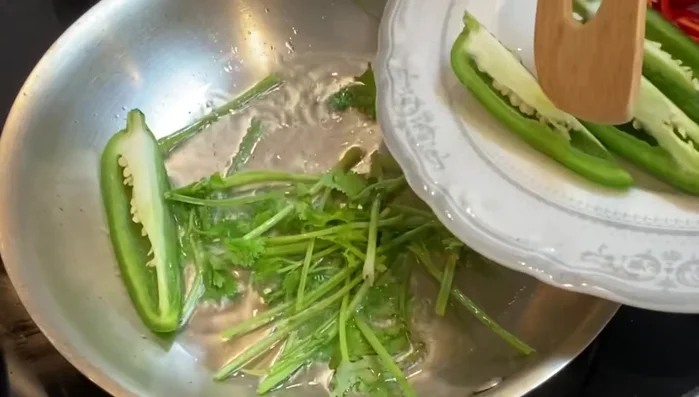 Place 3 tablespoons of oil in a skillet. Add cilantro stems, jalapenos, chili peppers, and sliced garlic.