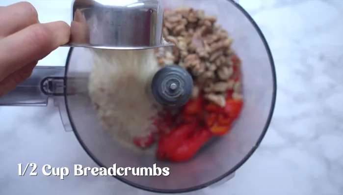 Add breadcrumbs, tahini, olive oil, lemon juice, smoked paprika, red pepper flakes, pomegranate molasses, and salt to the food processor.