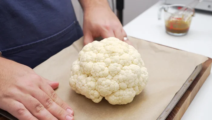 Coat cauliflower with spice rub. Add a whole head of garlic to the baking tray.