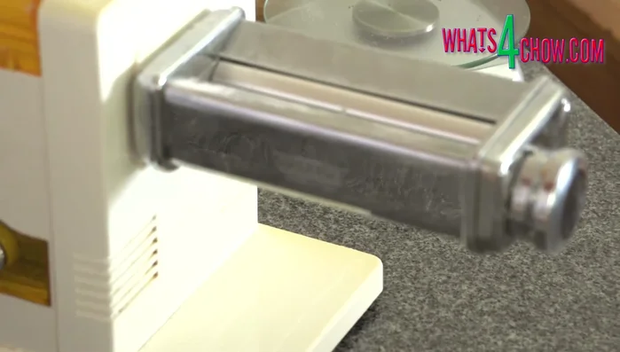 Divide the dough in half. Flatten one half and flour the outside if sticky. Pass it through a pasta roller on the widest setting, fold in half, and pass through again. Repeat until the dough is silky smooth, adding flour as needed.